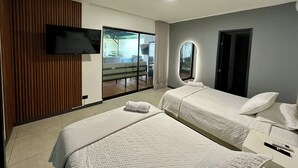 A hotel room with two beds, a TV, a large mirror, and a sliding glass door to a balcony.