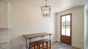 A room with a wooden table and benches, a hanging light fixture, and a door leading outside.