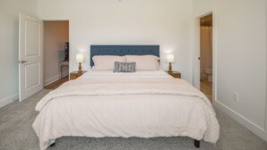A bedroom with a large bed, two bedside tables with lamps, a ceiling fan, and an open door leading to a bathroom.