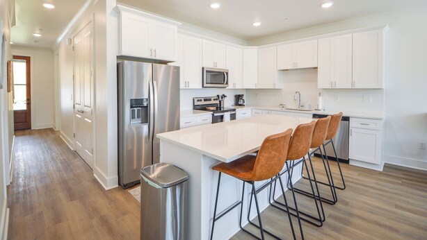 A modern kitchen with white cabinetry, stainless steel appliances, and a central island with bar stools.