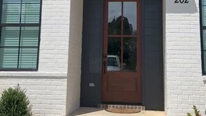 A modern two-story building with a dark brown front door, white brick walls, and a number '202' displayed above the door.