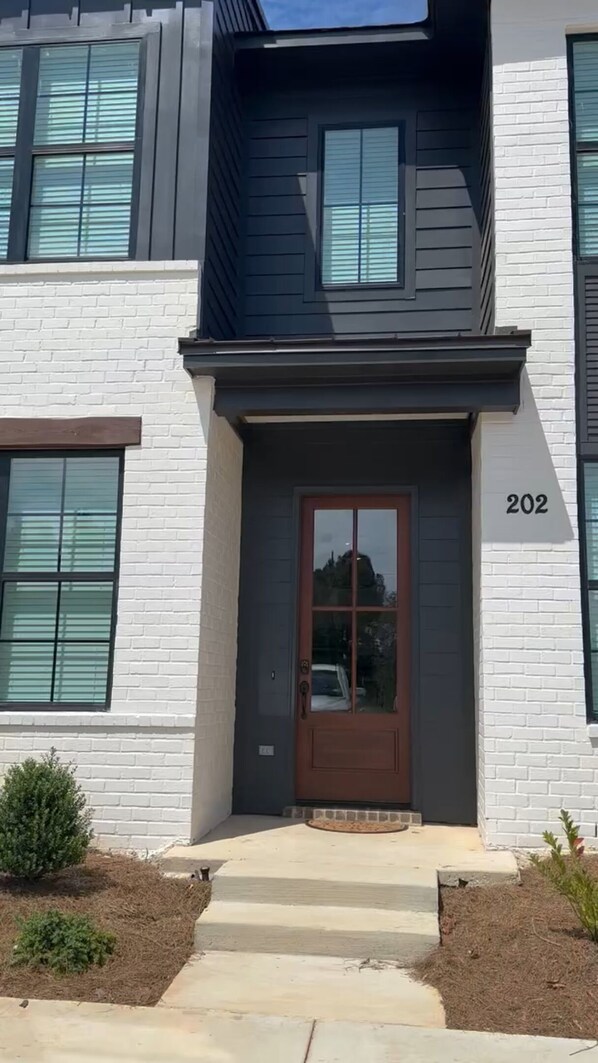 A modern two-story building with a dark brown front door, white brick walls, and a number '202' displayed above the door.