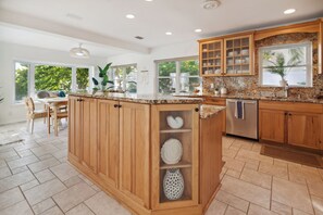 Enjoy cooking in this well-lit kitchen with a central island, dishwasher, and large window offering a view of the surrounding greenery.