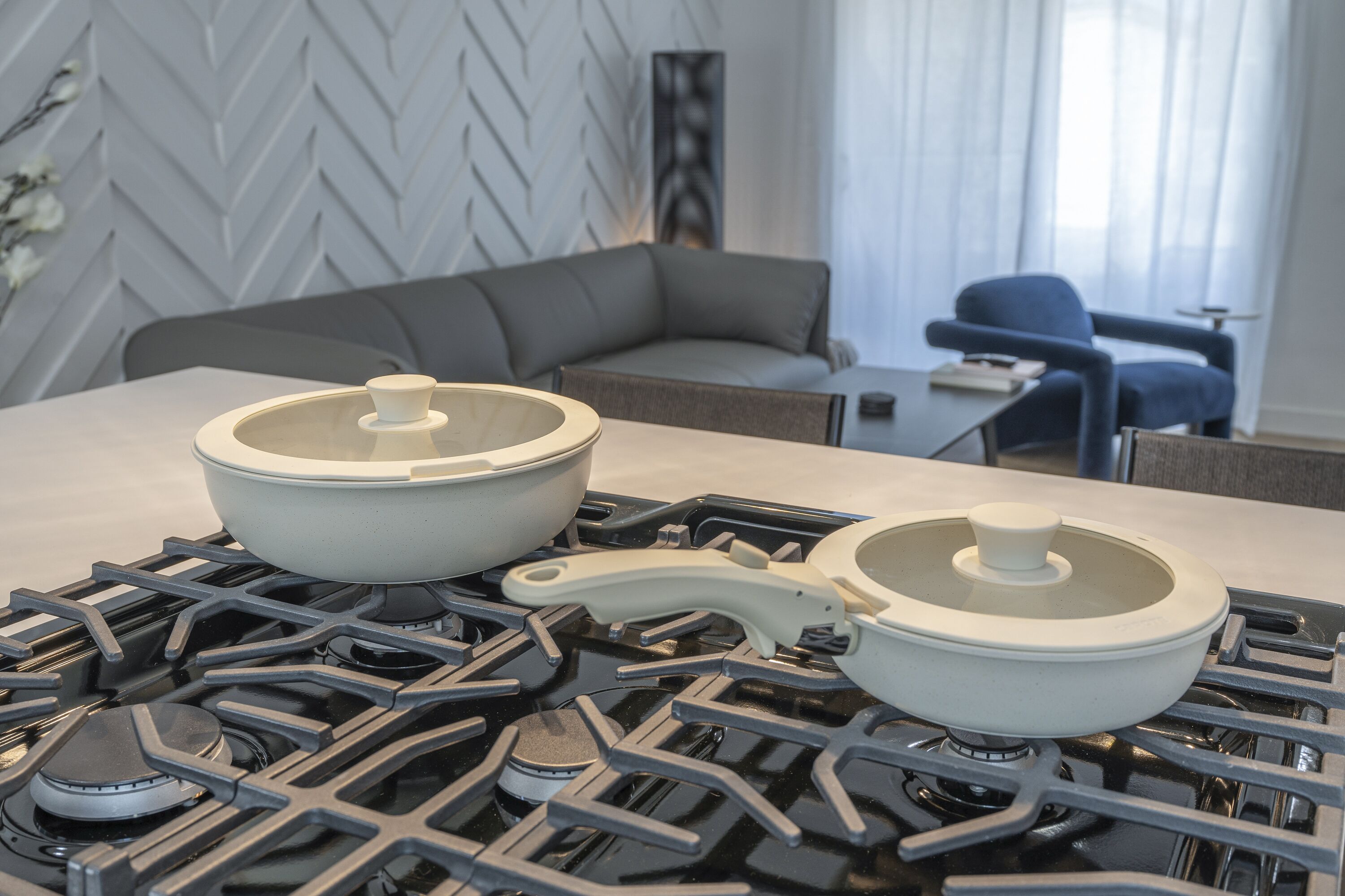 A kitchen with a modern stove, two pots, a chair, and a sofa in the background.