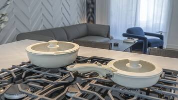 A kitchen with a modern stove, two pots, a chair, and a sofa in the background.