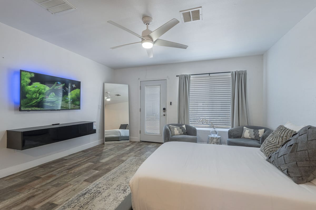 A modern bedroom with a bed, a TV mounted on the wall, a ceiling fan, and a window with curtains.