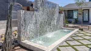 A spa area with a stone wall, a rectangular pool, and a small waterfall. - Ash & Ko Boutique Lodging (Phoenix)