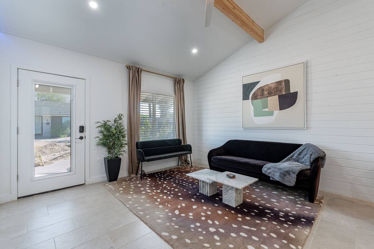 A modern living room with a black sofa, a coffee table, and a large abstract painting on the wall.
