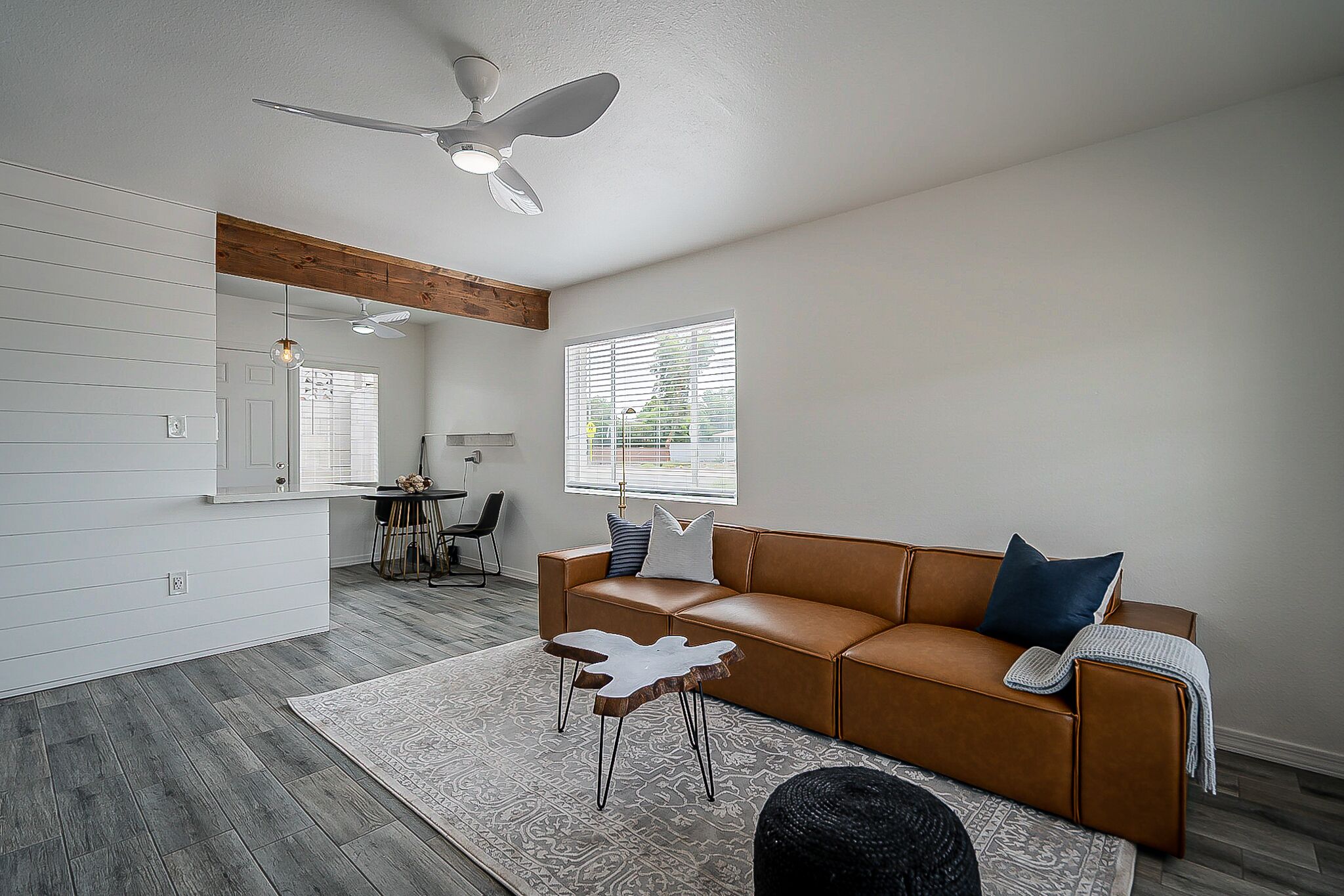A modern living room with a brown leather sofa, a white coffee table, and a ceiling fan.
