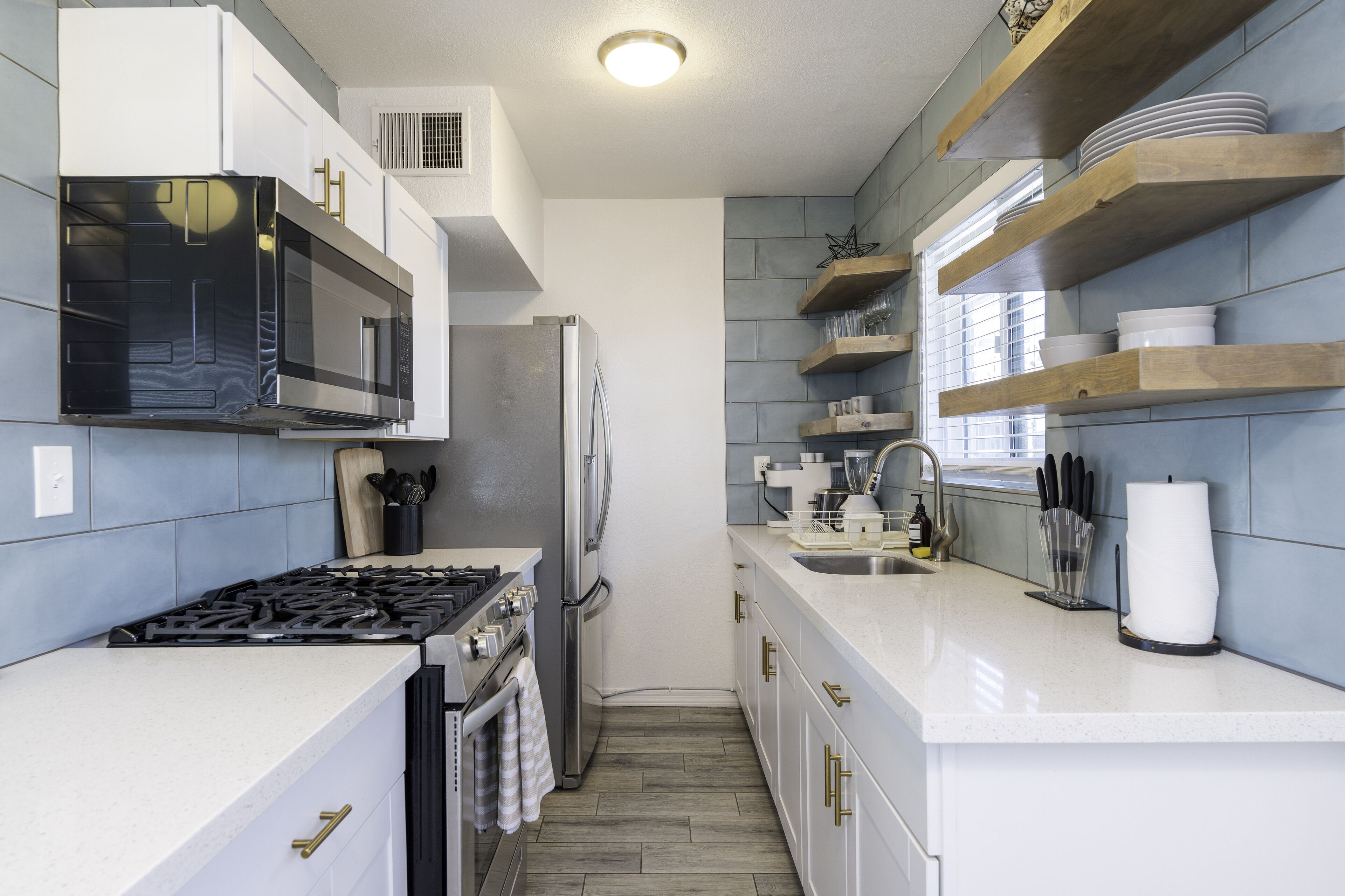 A modern kitchen with a gas stove, stainless steel appliances, and wooden shelves.