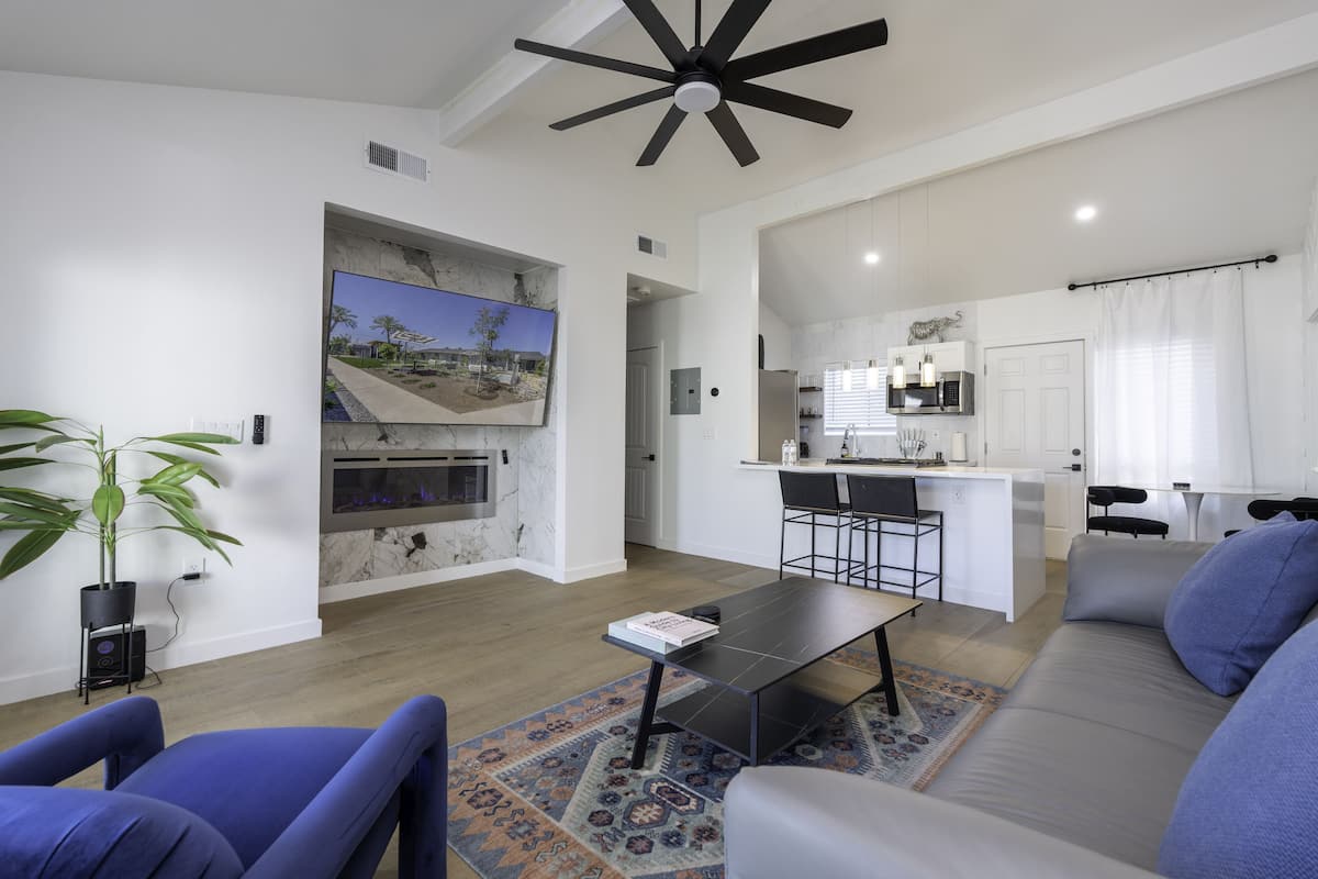 A modern living room with a sofa, a coffee table, and a TV. There is a kitchen area with a dining table and chairs.