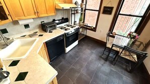 Een kleine keuken met een gasfornuis, spoelbak en houten keukenkastjes.
