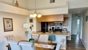A modern kitchen with wooden cabinets, a microwave, and a stove. There is a dining area with a table and chairs. - Grand Superior Condo 3BD Apartment Disney Parks (Kissimmee)