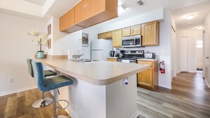 A modern kitchen with wooden cabinets, a central island with bar stools, stainless steel appliances, and a fire extinguisher. - Grand Superior Condo 3BD Apartment Disney Parks (Kissimmee)