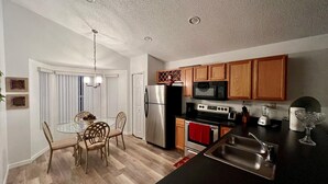 A modern kitchen with stainless steel appliances, wooden cabinets, and a dining area with a glass table and chairs. - Grand Luxury 4BD Pool Home Disney Universal (Davenport)