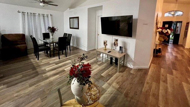 A modern living room with a dining area, a flat-screen TV mounted on the wall, and a ceiling fan. - Grand Luxury 4BD Pool Home Disney Universal (Davenport)