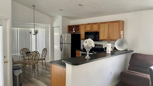 A modern kitchen with wooden cabinets, a stainless steel refrigerator, and a black microwave. - Grand Luxury 4BD Pool Home Disney Universal (Davenport)