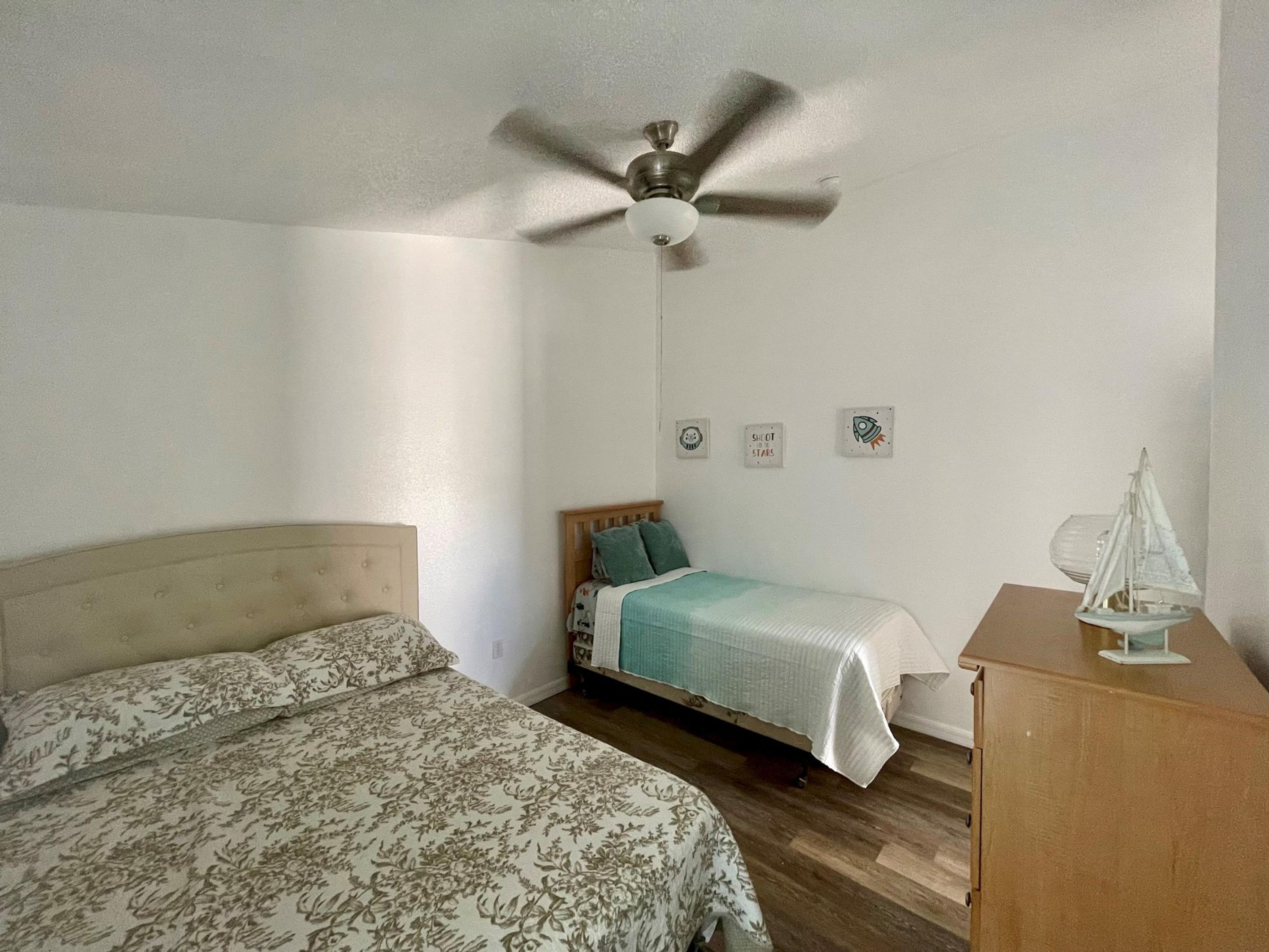 A bedroom with two beds, a ceiling fan, a wooden dresser, and a small sailboat model.