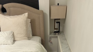Un letto ben rifatto con una testiera, un comodino con una lampada e un piano di lavoro in marmo.