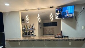 Eine Bar mit Marmorplatte, hängenden Pendelleuchten, einem an der Wand befestigten Fernseher und einem Flaschenregal.