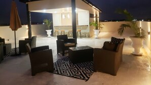 Eine Dachterrasse mit Außenbestuhlung, einem überdachten Bereich und Topfpflanzen.