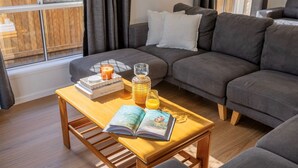 Een gezellige woonkamer met een grijze bank, een houten salontafel met een boek, een kaars en een glas sinaasappelsap.
