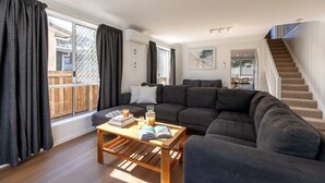 Een moderne woonkamer met een ruime hoekbank, een houten salontafel en een trap naar een bovenverdieping.