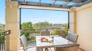 Ein Balkon mit einem Glastisch, gedeckt für zwei Personen, mit einer Champagnerflasche, einer Käseplatte und einer Weinflasche.