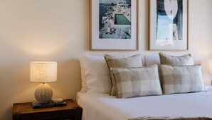 Ein ordentlich eingerichtetes Schlafzimmer mit einem Bett, Kissen, einem Nachttisch mit Lampe und zwei gerahmten Bildern an der Wand.