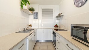 A modern kitchen with white cabinetry, a built-in oven, and a clock on the wall. - Craigmore 5 - Oceanfront Escape with Yamba's Best Beach Views - Holiday Yamba (Yamba)