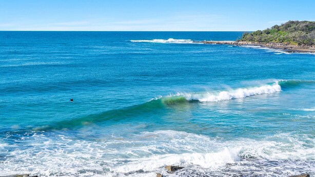 A coastal view with clear blue waters, a surfer, and a rocky shoreline. - Craigmore 5 - Oceanfront Escape with Yamba's Best Beach Views - Holiday Yamba (Yamba)