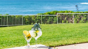 Two drinks on a table with a view of the ocean and a grassy area. - Craigmore 5 - Oceanfront Escape with Yamba's Best Beach Views - Holiday Yamba (Yamba)