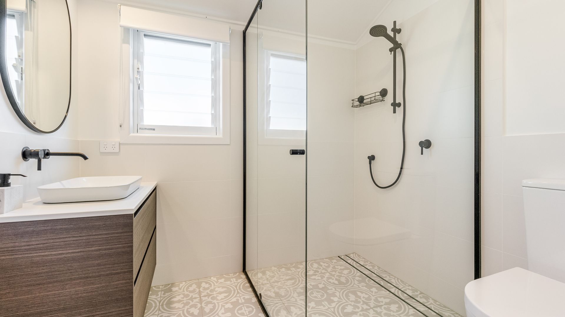 A modern bathroom with a glass shower enclosure, a white sink, and a window providing natural light.