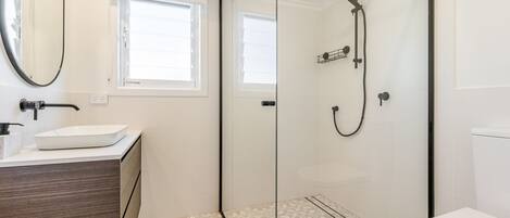 A modern bathroom with a glass shower enclosure, a white sink, and a window providing natural light.