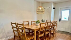 A dining area with a wooden table and chairs, a hanging light fixture, and a door in the background. - Lamplight Cottage | paddle-boards, AC, best beach! (Sylvan Lake)