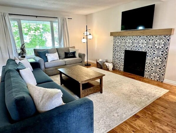 A living room with a sectional sofa, a coffee table, a fireplace, and a television mounted above it.