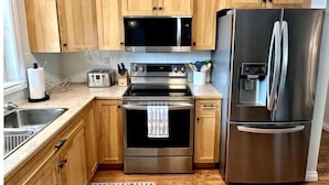 A kitchen with wooden cabinets, a stainless steel refrigerator, a microwave, a toaster, and a stove. - Lamplight Cottage | paddle-boards, AC, best beach! (Sylvan Lake)