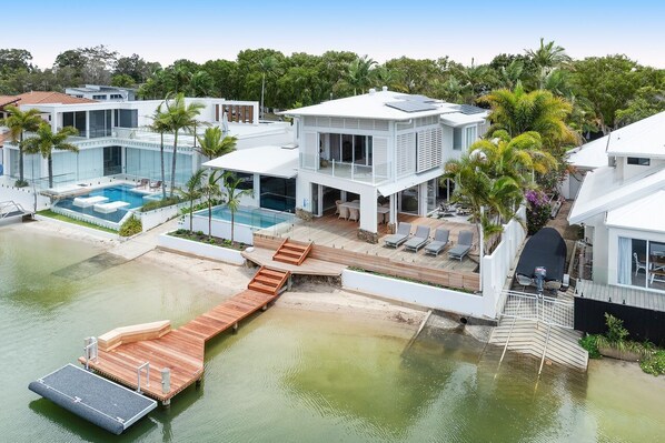 Une propriété moderne située au bord de l’eau, dotée d’une piscine, d’une terrasse en bois et de plusieurs bâtiments.