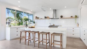 Una cucina moderna con un'isola grande, mobili bianchi e vista su palme.