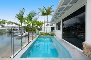 Une piscine avec vue sur un port de plaisance, entourée de palmiers et bordée d’une architecture moderne.