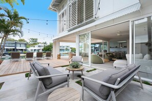 Une terrasse extérieure dotée de mobilier moderne, une porte vitrée donnant sur un espace abrité et une vue sur le quartier environnant.