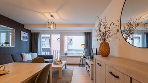 A modern living room with a wooden dining table, a sofa, and a large mirror. There is a balcony with a view of the city. - Amuzee with parking & lateral sea view by Interhome (Blankenberge)