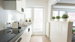 A modern kitchen with white cabinetry, a black countertop, and a view of the outside through a large window. - Amuzee with parking & lateral sea view by Interhome (Blankenberge)