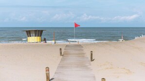 A beach with a wooden walkway leading to a lifeguard tower and a red flag. - Amuzee with parking & lateral sea view by Interhome (Blankenberge)