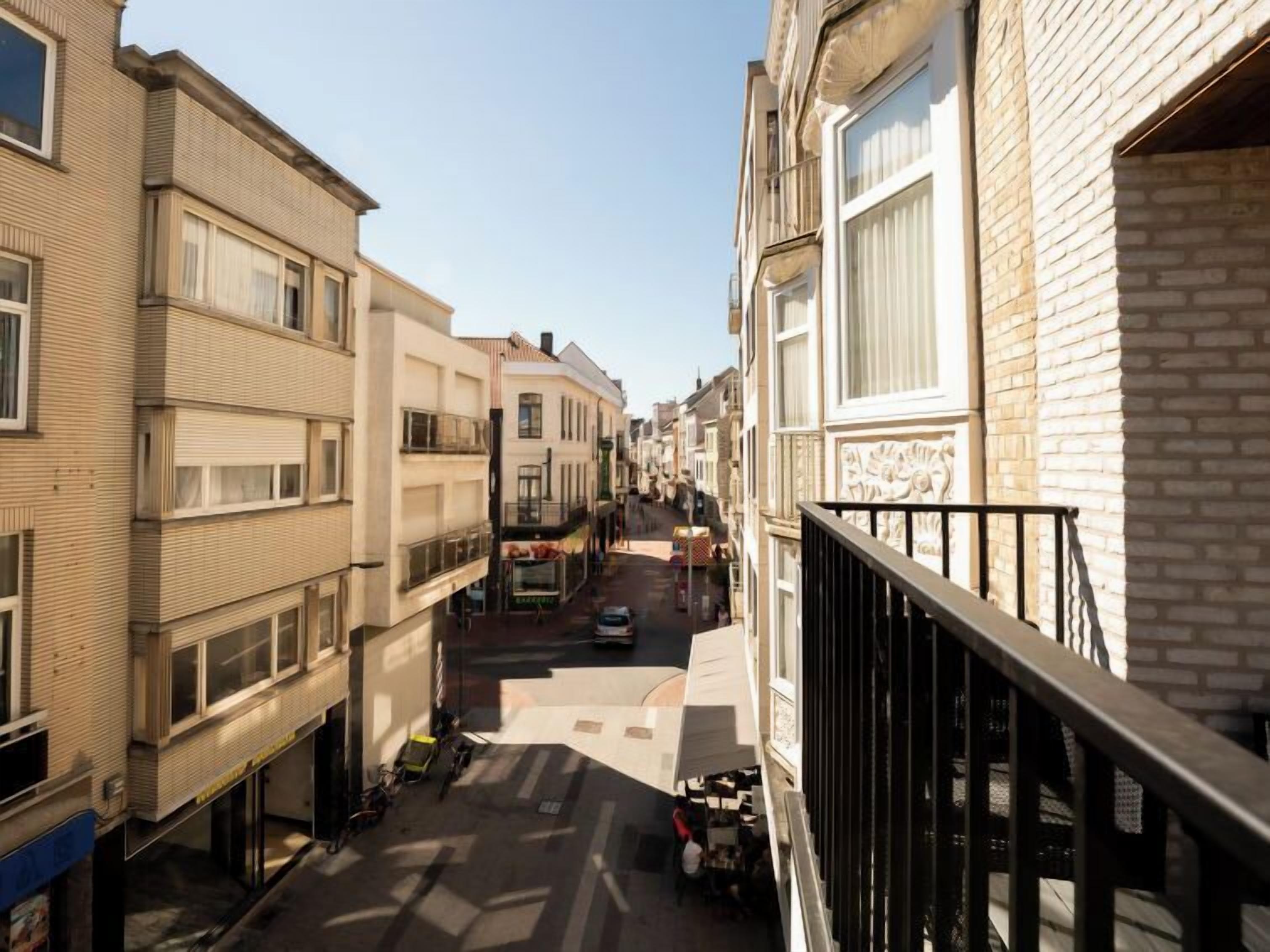 Uma rua estreita com edifícios em ambos os lados, com varandas e céu claro.