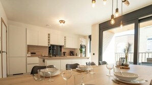 Een moderne keuken met witte kasten, een houten eettafel voor vier personen en hanglampen.