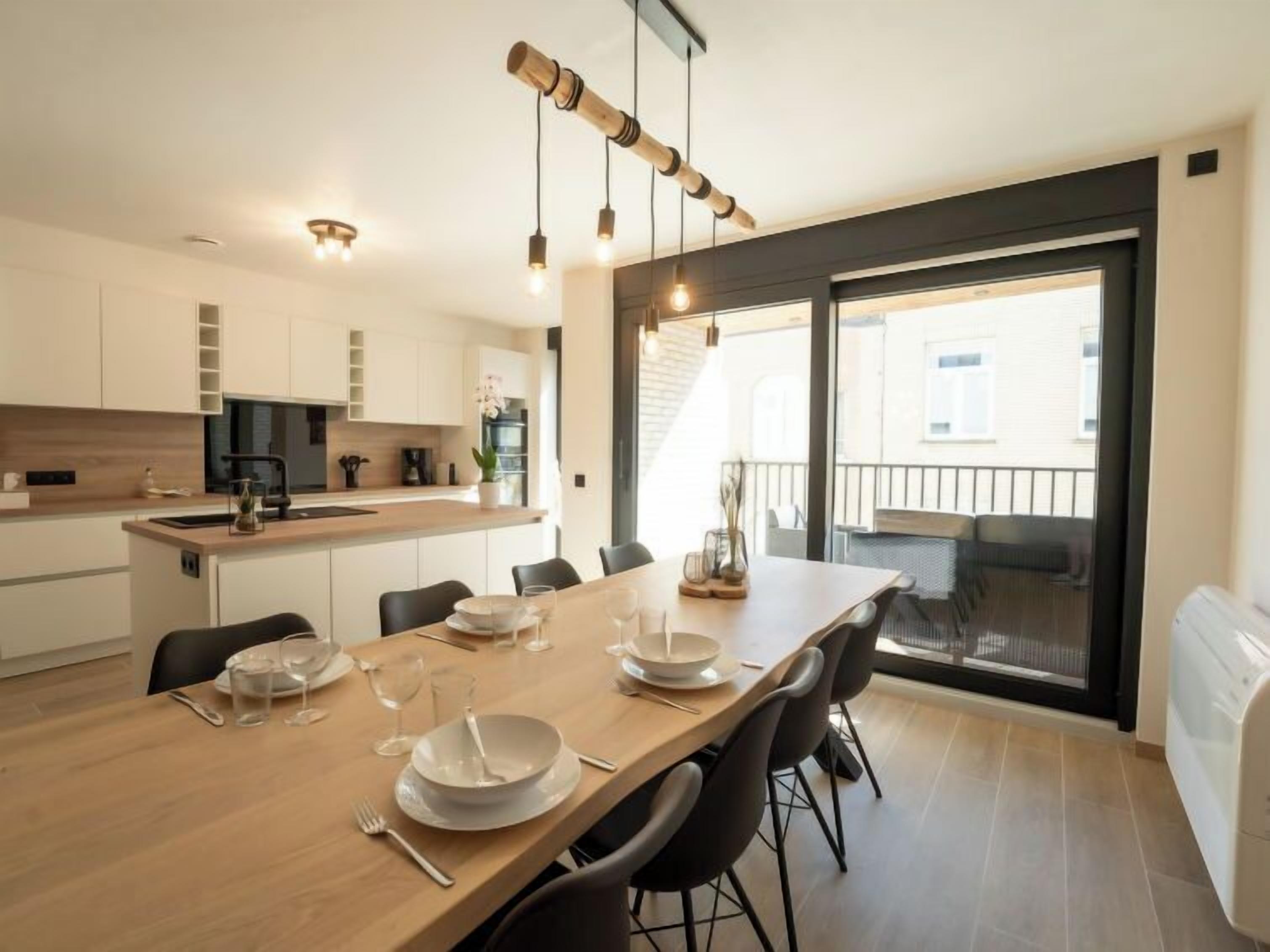 A modern kitchen with white cabinets, a wooden dining table set for four, and a large sliding glass door leading to a balcony.
