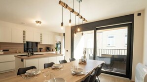 Een moderne keuken met witte kastjes, een houten eettafel gedekt voor vier personen en een grote glazen schuindeur die naar een balkon leidt.