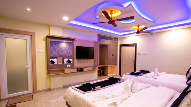 Habitación de hotel con dos camas, ventilador de techo, televisión y un minibar.