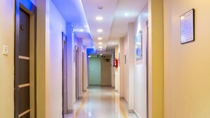 Pasillo de hotel con puertas a ambos lados, una franja amarilla en el suelo y un extintor en la pared.